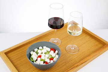 Drewniana taca z lampkami wina czerwonym i białym obok w miseczce kostki sera z warzywami, całośc na białym tle - obrazy, fototapety, plakaty