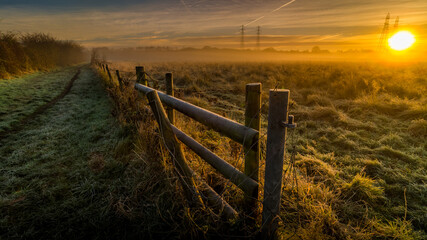 Obraz premium Frosty Frozen wooden fence with Autumn grassland and sunrise