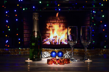 Two glasses and a bottle of champagne on the table.
Christmas New Year decorations, fireplace. Fire, wood.