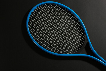 Tennis racket on black background, top view. Sports equipment