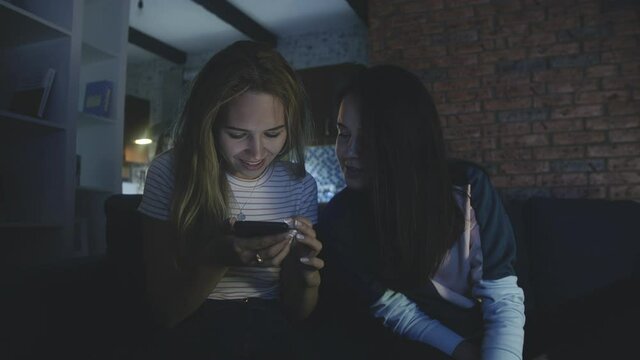 Happy friends sitting on sofa and looking at screen of mobile phone or smartphone. Quarantine using modern technology. Connecting through social networks or messages during epidemic. phubbing concept.