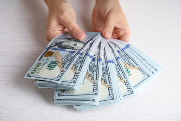 Woman holding dollar banknotes at white wooden table, closeup