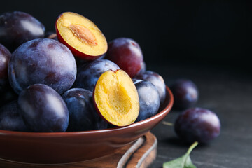 Delicious ripe plums in bowl on black table, closeup