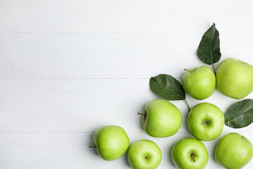 Obraz premium Ripe green apples and leaves on white wooden table, flat lay. Space for text