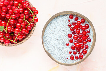 Fresh red currant berries and overnight chia seed pudding in a coconut bowl. Close up, top view, flat lay. Healthy raw food concept. Pink background, copy space.