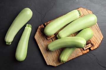 Raw green zucchinis and wooden board on black slate table, flat lay