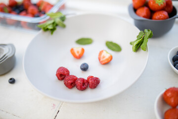 Smiling face made with berries and mint leaves on a plate