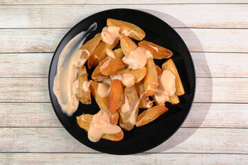 French fries with Cabrales cheese sauce in black plate on wooden table
