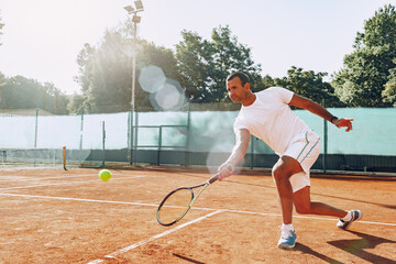 Fit man plays tennis on tennis field