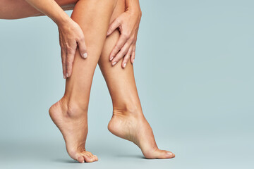 Cropped shot of a woman touching her legs with smooth, silky and soft skin after making a depilation, sitting over blue background