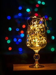 Crystal wine glasses with golden glowing garland on Christmas table bokeh light background Vertical screensaver. Romantic New Years eve dinner champagne couple in love.Magic winter holidays atmosphere