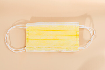 Top view of yellow surgical face protection mask isolated on beige color background.