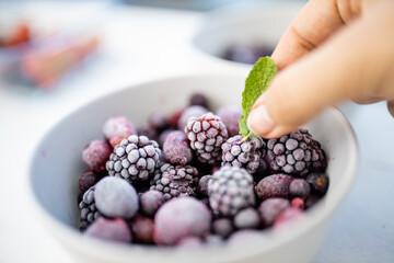 Female hand holding a mint leaf on a bowl of blackberries