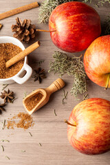 Top view of red royal gala apples with cinnamon sticks, brown sugar and autumn leaves, with selective focus, on wooden board, in vertical, with copy space