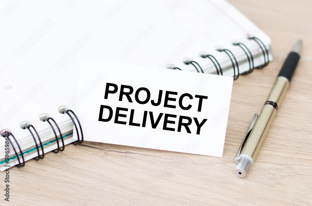 Aufkleber business card with project delivery text on the table, next to a notebook and a pen.