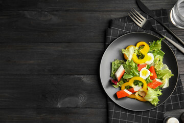 Salad with crab sticks and lettuce served on black wooden table, flat lay. Space for text