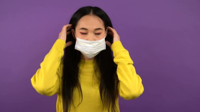 young asian woman wearing protective medical mask. lady in yellow sweater on purple isolated background. 4K