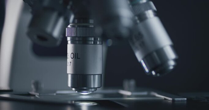 Close-up shot of sample slide and microscope with metal lens at laboratory.