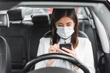  woman in medical mask messaging on smartphone in car on blurred foreground