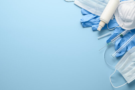 Used disposable medical face masks, latex gloves, syringes, test tubes on pastel blue background. Problem of environmental pollution during pandemic of coronavirus COVID-19. Flat lay, copy space