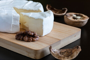 Soft cheese with mold with a cut segment and walnut kernels on a wooden serving Board.