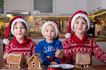 Children, boys, decorating home made ginger bread houses at home with mom helping