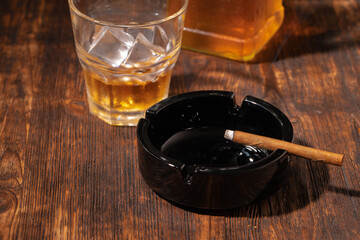 Glass of whisky and lighted cigar in an ash tray