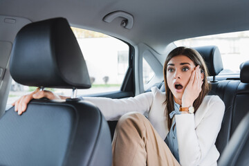  woman holding hand on face while sitting on back seat of car on blurred foreground