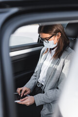 businesswoman in mask using digital tablet while riding in car on blurred foreground