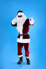 Fototapeta na wymiar Full length portrait of Santa Claus with sunglasses on light blue background