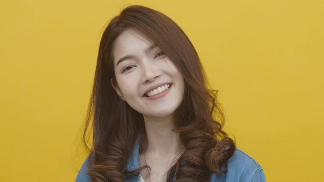 Portrait of asian young woman wearing white t-shirt and blue jean jecket feeling happy, funny, enjoy and looking at camera with joyful and charming smile. Asian woman on yellow background studio shot
