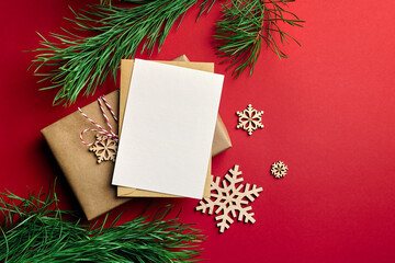 Christmas greeting card mockup with gift box, snowflakes decorations and pine tree branches on red paper background