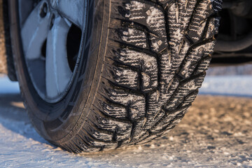 Car wheel with winter studded tread on snowy road.