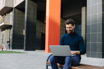 Smiling bearded man working on laptop on fresh air