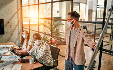 Workers discuss and meet while wearing a medical mask to protect against the corona virus. A young man writes a mind map on a whiteboard and makes new business plans during the COVID-19 pandemic.