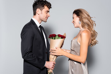  young man gifting bouquet to woman isolated on grey