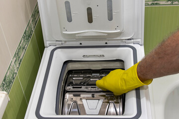 A man's hand opens a top-loading washing machine.