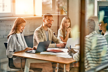 Young professional team. Group of young modern people in elegant casual clothes are brainstorming while sitting behind glass wall in creative office