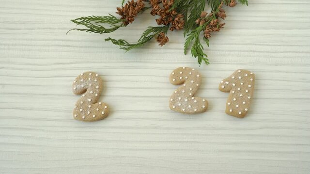 A man's hand changes zero in 2021 to a gingerbread in a mask. Rustic Christmas 2021. Christmas background with fir branches and decorations
