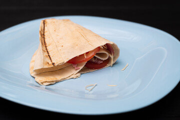 Tortilla with cheese and ham. Pita with grated cheese, ham, tomatoes on a plate.