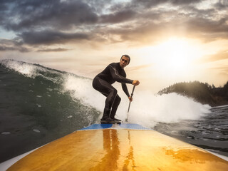 Adventurous Man Surfing the waves at the Pacific Ocean in Oregon Coast. Dramatic Colorful Sunset...