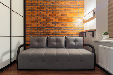 Modern minimalist small room interior in loft design style with sofa, brick wall, wooden shelf and lamp
