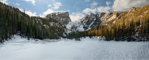 Stunning panorama of Dream Lake in Rocky Mountain National Park with snow covered peaks surrounded by a forest of trees, snow, and ice.