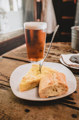 a piece of tortilla on a plate, with a pair and a fork, with a cold beer, on a rustic wooden table in a bar.