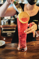 a woman with a face mask preparing a cuba libre with alcohol in a pub. Red drink in a very large glass. night life and party concept