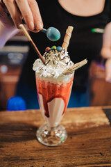 an unfocused person preparing a handmade smoothie in a bar with many colors. A large crystal goblet on a wooden table.