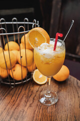 orange juice on a wooden table in a bar, with ice and cream. Refreshing drink in a glass. A basket of oranges. Healthy fruit diet.