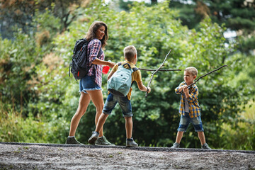 Mother and her little sons hiking trough forest .Making fun and fight with wooden sticks.	
