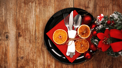 Christmas dinner decoration with dried oranges and a red napkin on a black plate. Artificial Christmas tree on wooden background