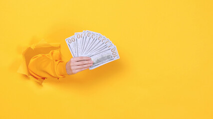 Close up woman hand arm holding fan of cash money in dollar banknotes isolated through torn yellow background studio Copy space advertisement place for text image Advertising area workspace mock up